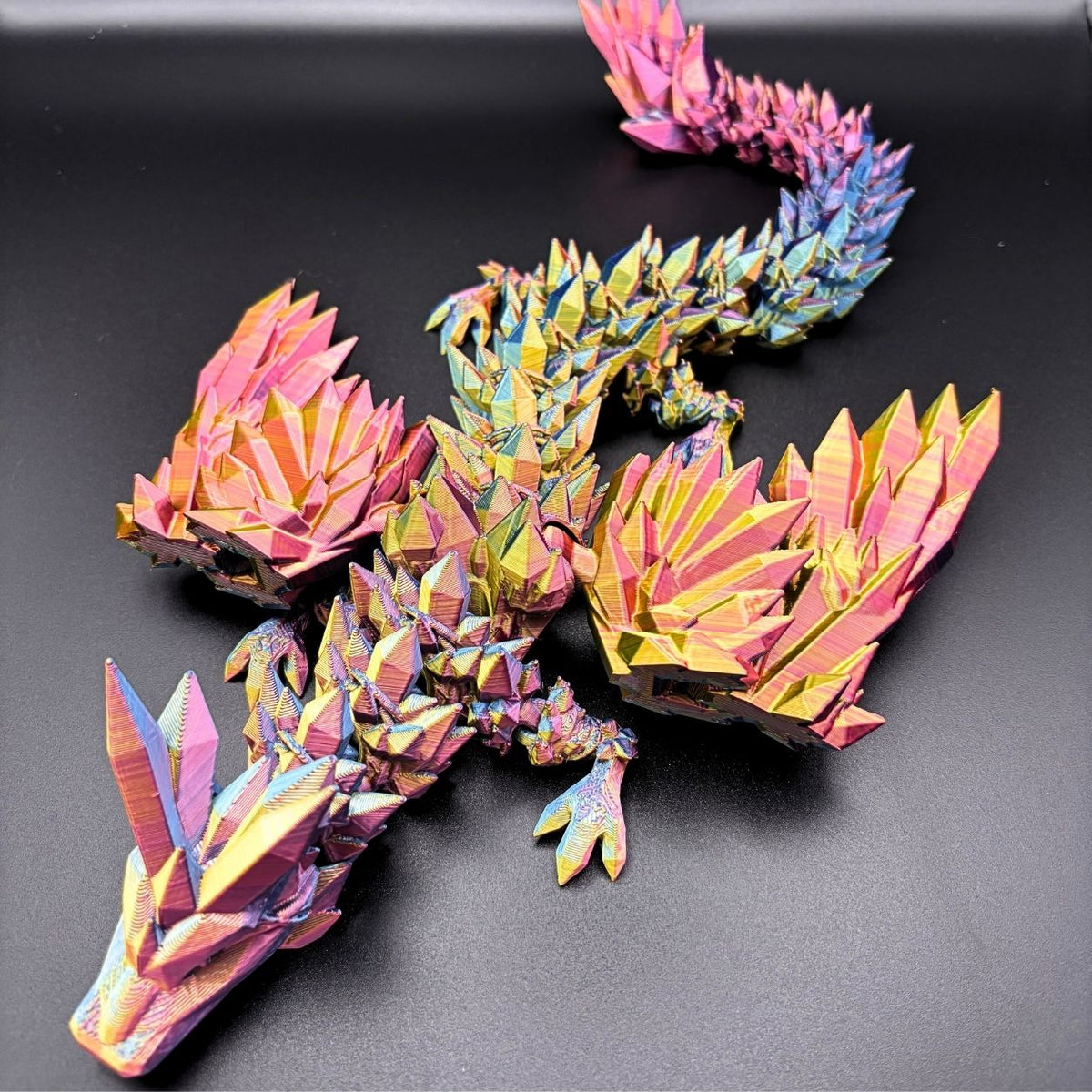 A colorful 3D papercraft dragon model with a metallic iridescent finish, displayed on a dark gray background.